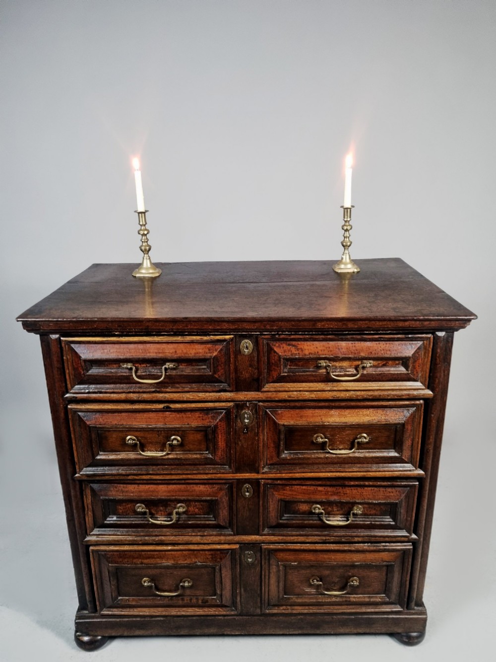 A seventeenth-century dark oak chest of drawers featuring geometric mitred drawer panels, brass swing handles, and turned bun feet. View III