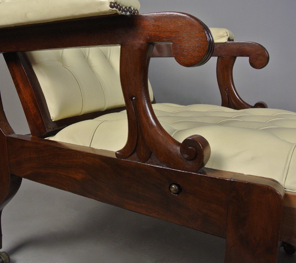 A Regency mahogany reclining armchair featuring cream button-tufted leather upholstery, scroll arms, and turned front legs on brass castors. View III