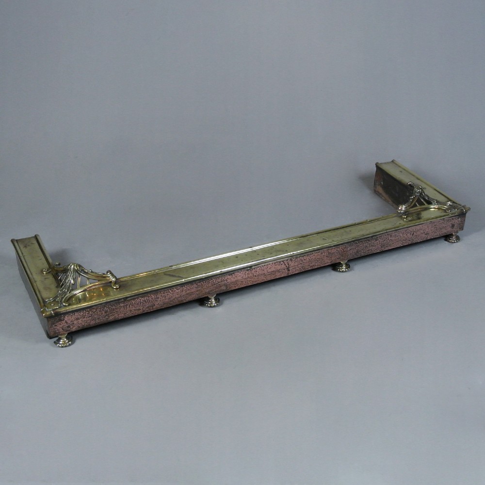 An Art Nouveau fire fender made of hammered copper with a polished brass top rail, corner mounts, and small rounded feet.