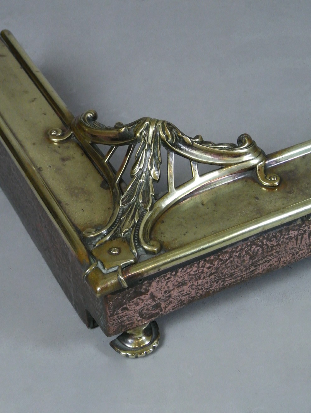 An Art Nouveau fire fender made of hammered copper with a polished brass top rail, corner mounts, and small rounded feet. View III