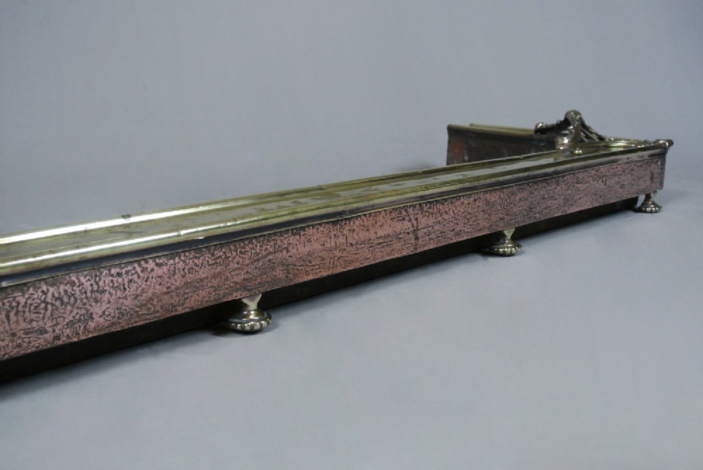 An Art Nouveau fire fender made of hammered copper with a polished brass top rail, corner mounts, and small rounded feet. View IV