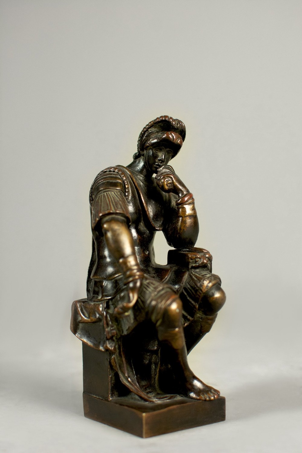 A dark patinated bronze figure depicting Lorenzo de Medici seated in a thoughtful pose on a rectangular base.