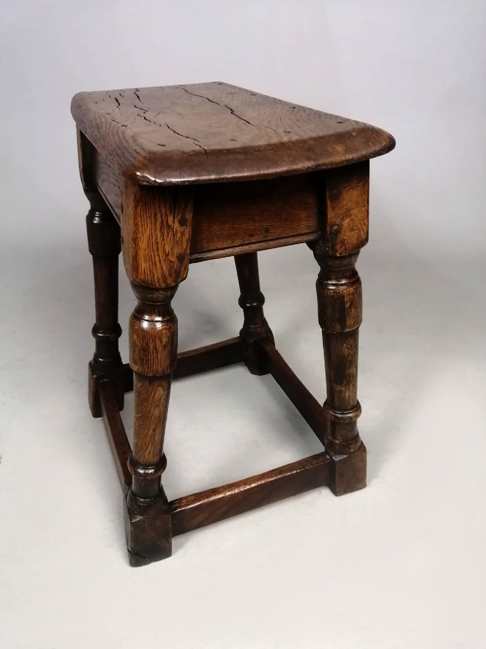An antique dark brown oak joint stool with an elm top, turned legs, and perimeter box stretchers. View IV