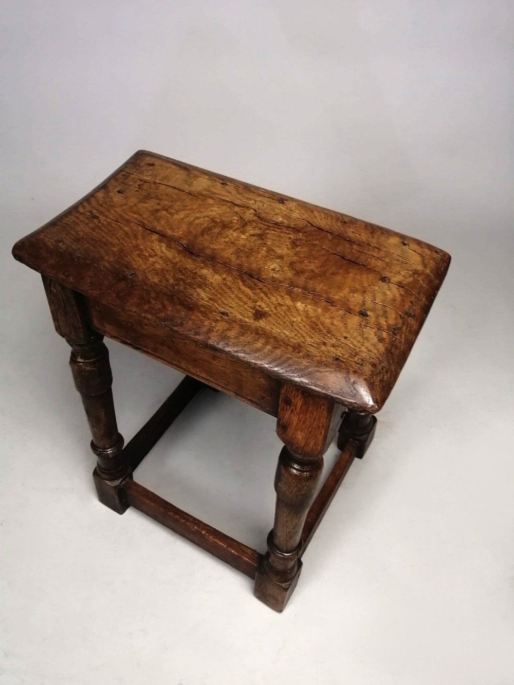 An antique dark brown oak joint stool with an elm top, turned legs, and perimeter box stretchers. View V
