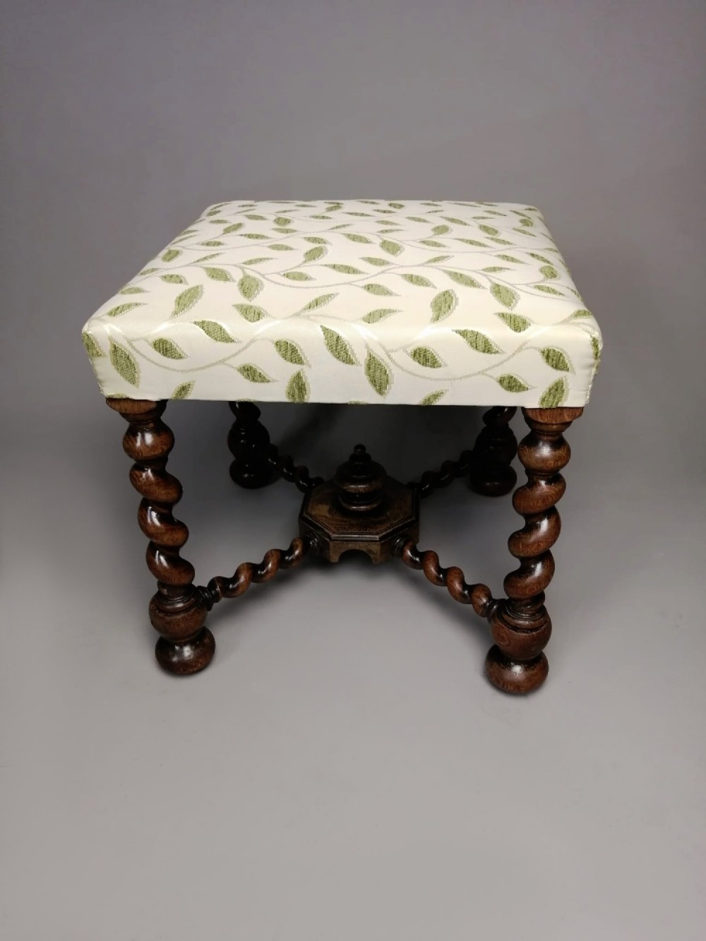 A square dark walnut stool featuring spiral barley twist legs, a central finial stretcher, and cream upholstery with embroidered green leaf motifs. View II