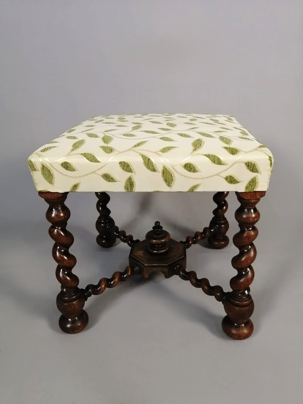 A square dark walnut stool featuring spiral barley twist legs, a central finial stretcher, and cream upholstery with embroidered green leaf motifs. View III