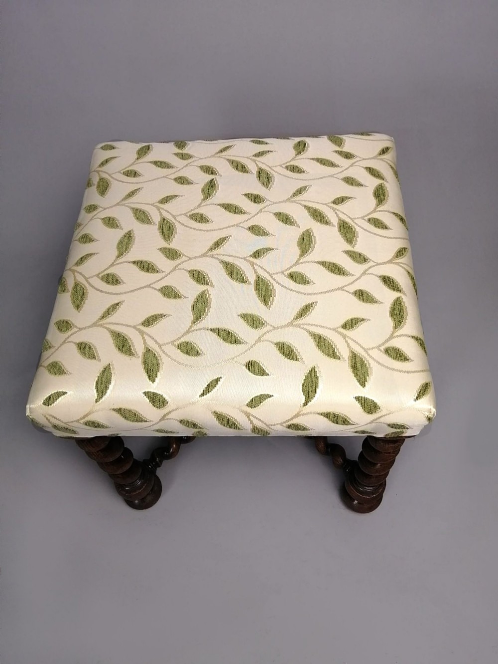A square dark walnut stool featuring spiral barley twist legs, a central finial stretcher, and cream upholstery with embroidered green leaf motifs. View IV