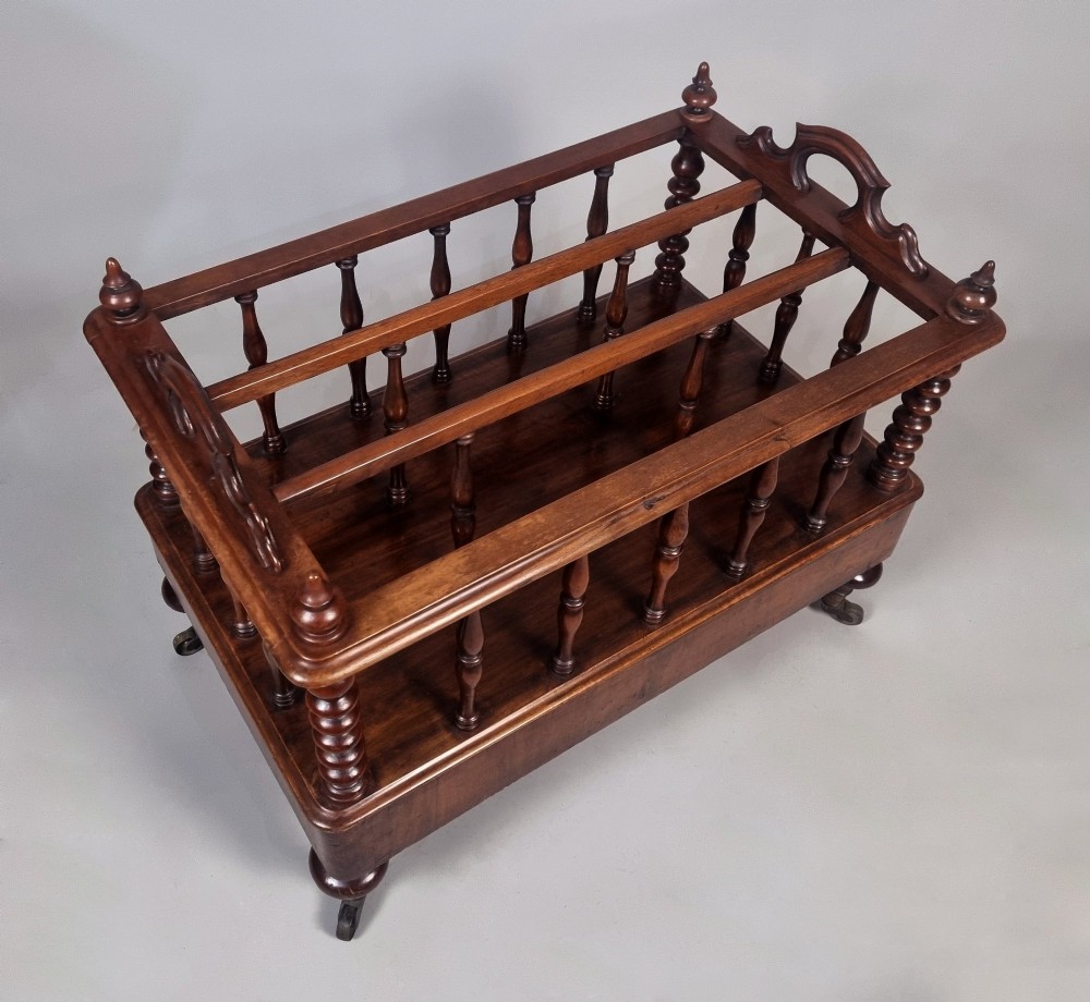 A Victorian walnut Canterbury featuring vertical spindle dividers, a lower drawer base, carved side handles, and turned feet with brass castors. View VII