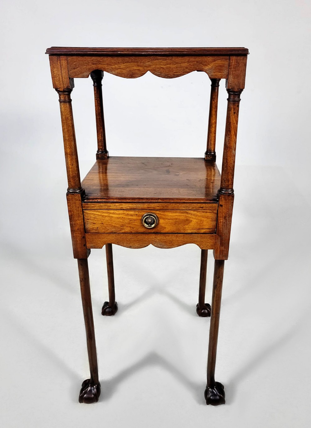 An antique George III Cuban mahogany nightstand featuring tiered shelves, a central drawer, turned column supports, scalloped aprons, and carved claw and ball feet.