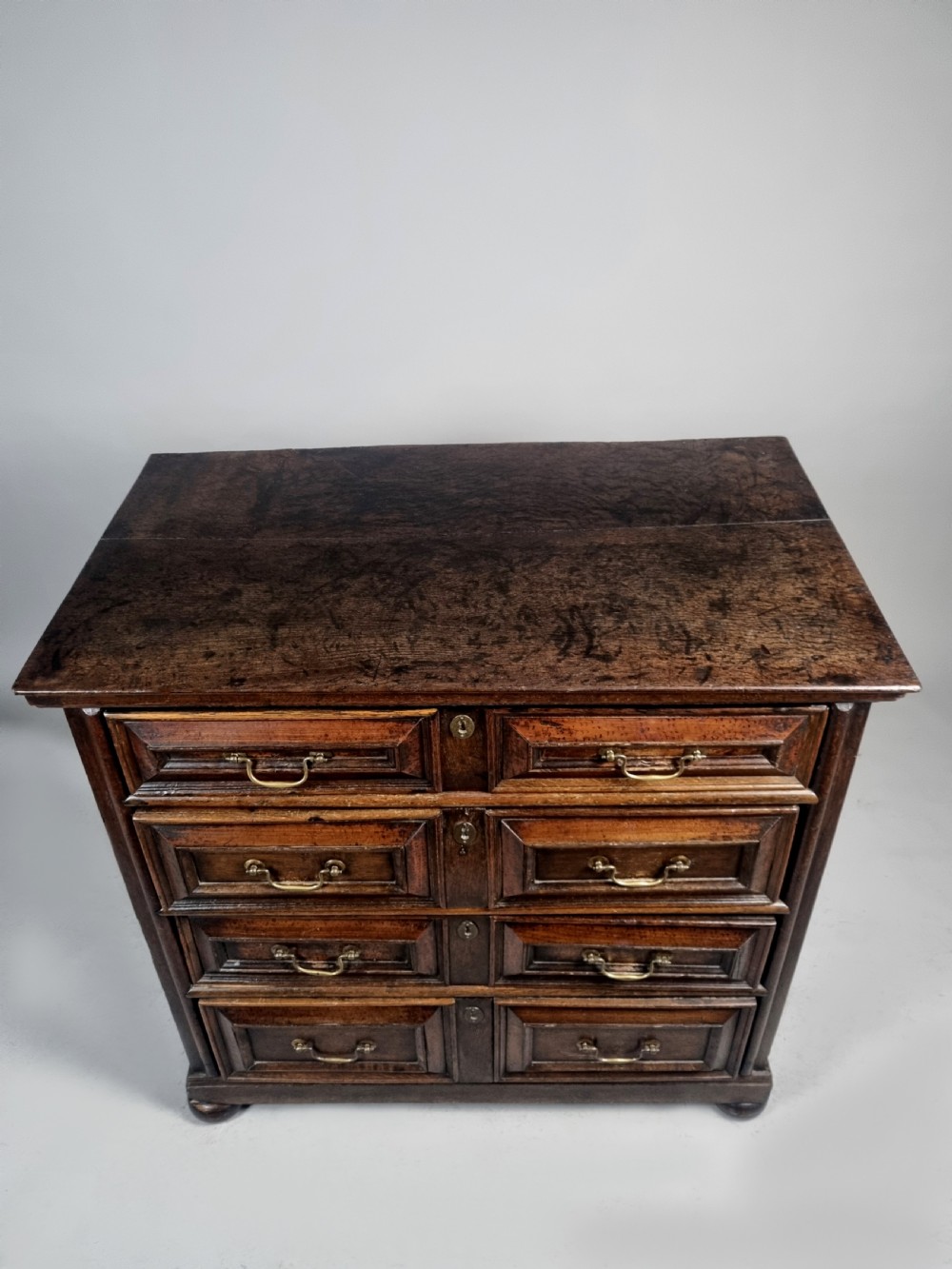A seventeenth-century Charles II solid oak chest of drawers featuring geometric panelled drawer fronts, brass drop handles, and bun feet. View IV