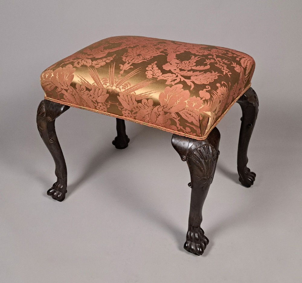 An 18th-century Irish George II mahogany footstool with shell-carved cabriole legs, claw and ball feet, and patterned damask top. View V