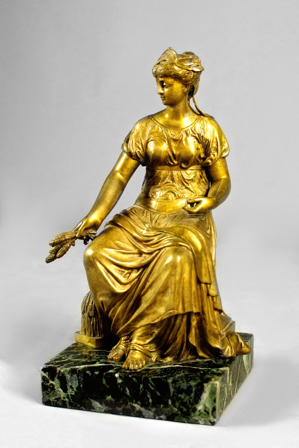 A nineteenth-century gilt bronze sculpture depicting the seated Roman goddess Ceres holding a sheaf of wheat on a square green marble base.