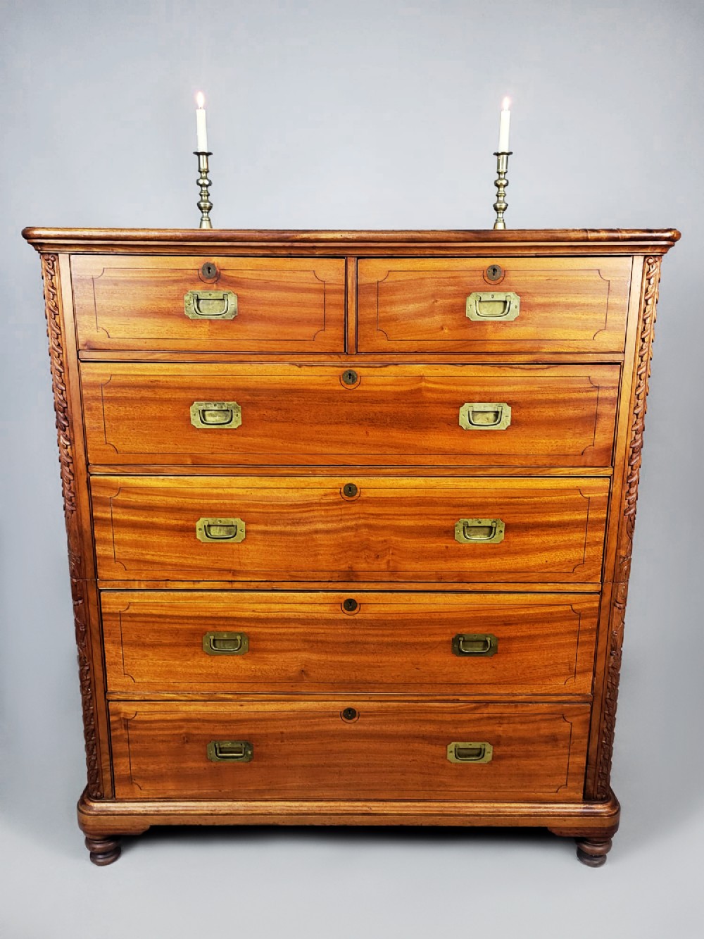 A nineteenth-century teak campaign chest of drawers featuring flush brass handles, keyholes, two short over three long drawers, and carved side pilasters. View VII