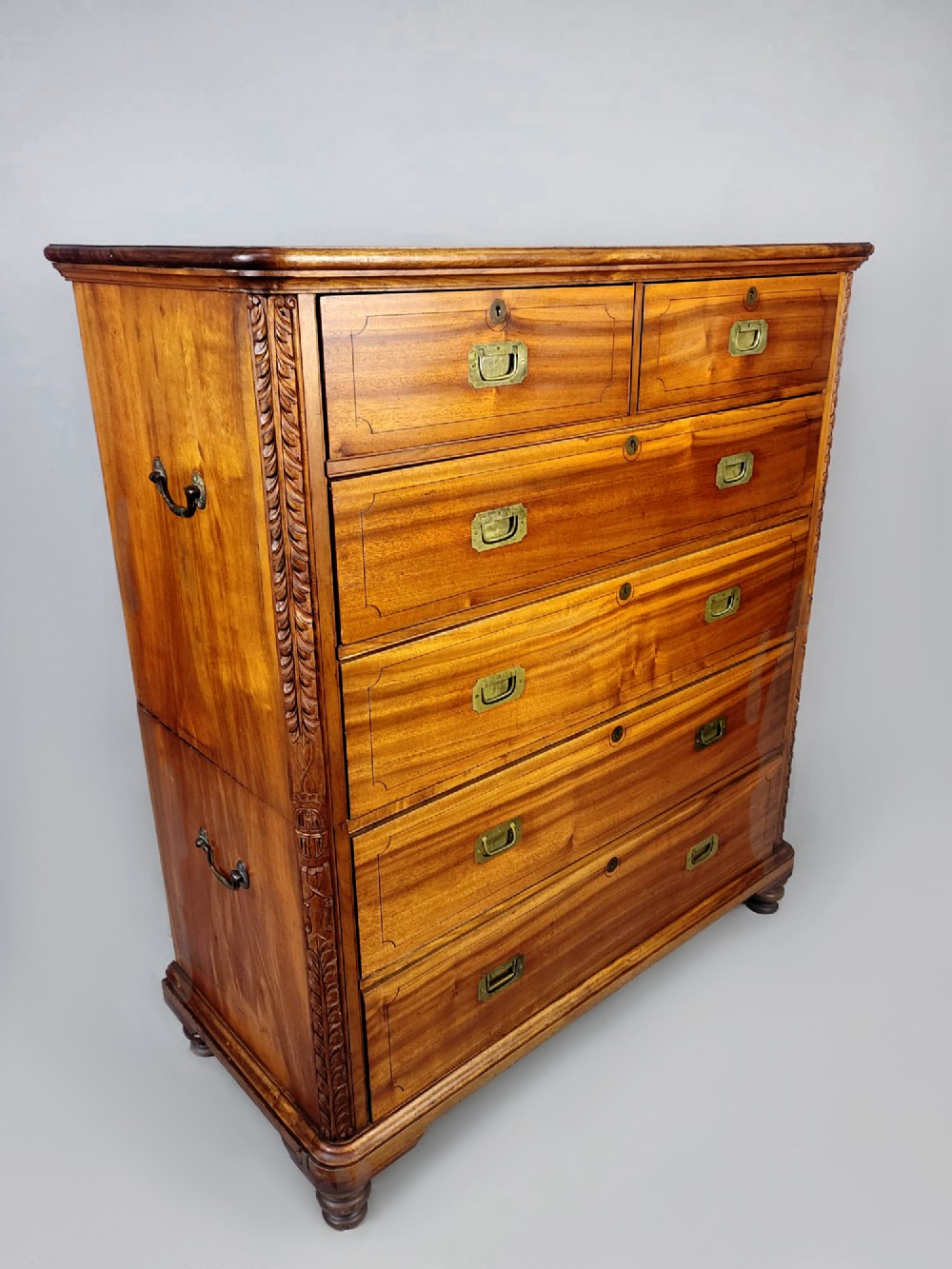 A nineteenth-century teak campaign chest of drawers featuring flush brass handles, keyholes, two short over three long drawers, and carved side pilasters. View VIII