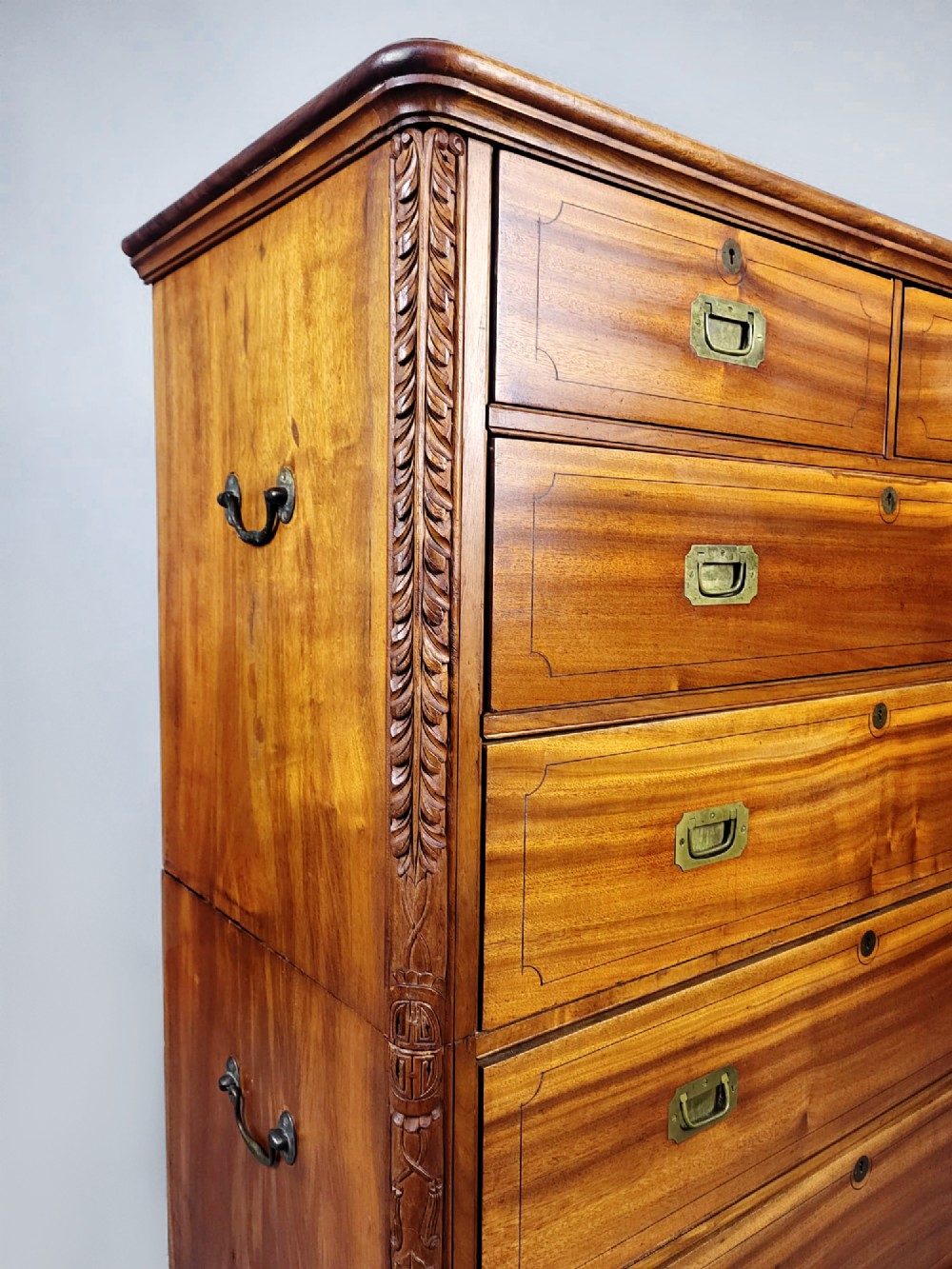A nineteenth-century teak campaign chest of drawers featuring flush brass handles, keyholes, two short over three long drawers, and carved side pilasters. View X