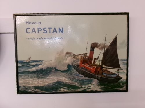 A framed vintage cardboard advertisement for Capstan cigarettes featuring a steam vessel navigating rough seas under text reading Have a Capstan. View II