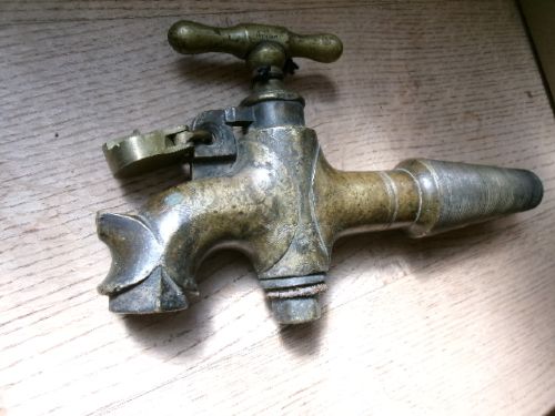 A heavy Victorian brass barrel tap featuring a tapered shaft, curved spout, T-bar handle, and an integrated locking loop mechanism. View VI