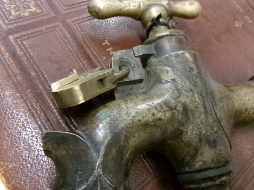 A heavy Victorian brass barrel tap featuring a tapered shaft, curved spout, T-bar handle, and an integrated locking loop mechanism. View VIII