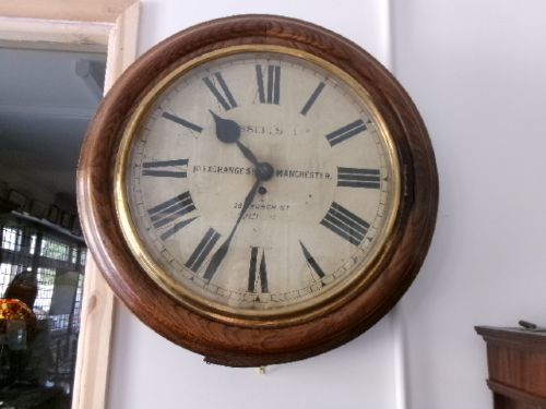 A circular antique wall clock housed in a thick moulded oak case with a glazed brass bezel and painted dial displaying Roman numerals. View VII
