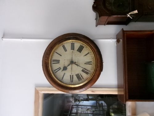 A circular antique wall clock housed in a thick moulded oak case with a glazed brass bezel and painted dial displaying Roman numerals. View XI