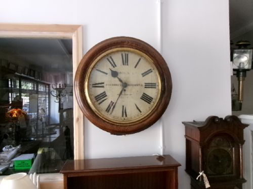 A circular antique wall clock housed in a thick moulded oak case with a glazed brass bezel and painted dial displaying Roman numerals. View XII