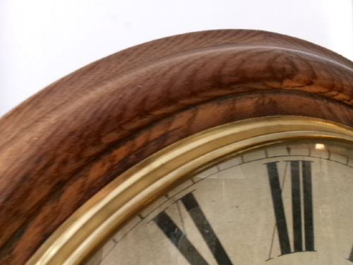 A circular antique wall clock housed in a thick moulded oak case with a glazed brass bezel and painted dial displaying Roman numerals. View XIII