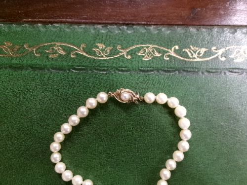 A single strand of white cultured pearls with a 9ct gold clasp displayed inside a dark brown presentation case. View III
