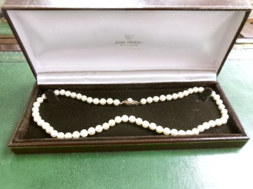 A single strand of white cultured pearls with a 9ct gold clasp displayed inside a dark brown presentation case. View V