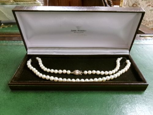 A single strand of white cultured pearls with a 9ct gold clasp displayed inside a dark brown presentation case. View VII