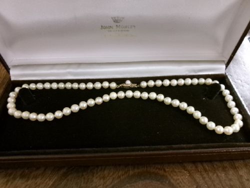A single strand of white cultured pearls with a 9ct gold clasp displayed inside a dark brown presentation case. View X