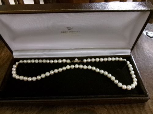 A single strand of white cultured pearls with a 9ct gold clasp displayed inside a dark brown presentation case. View XI