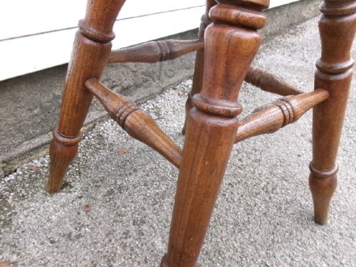 An antique Victorian wooden tavern stool featuring a circular thick elm seat and turned splayed legs joined by stretchers. View V