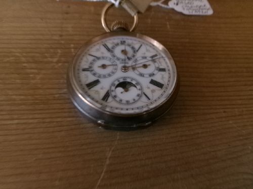 A gunmetal calendar moonphase pocket watch with an enamel dial displayed upright inside a turned wooden holder. View II