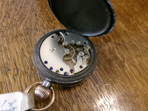 A gunmetal calendar moonphase pocket watch with an enamel dial displayed upright inside a turned wooden holder. View VIII