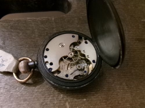 A gunmetal calendar moonphase pocket watch with an enamel dial displayed upright inside a turned wooden holder. View IX