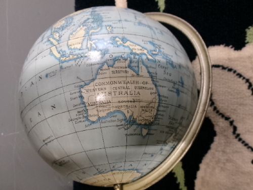 A vintage tinplate world globe with a pale blue lithographed ocean map mounted on a circular metal base with a curved semi-meridian arm. View III