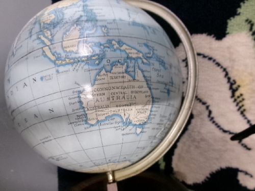 A vintage tinplate world globe with a pale blue lithographed ocean map mounted on a circular metal base with a curved semi-meridian arm. View IV