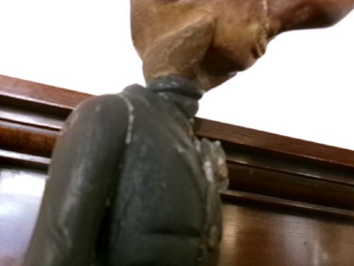 A carved and painted wooden figure of a caricatured man wearing a top hat and tailcoat, holding an umbrella while standing on a rounded grey base. View XIV
