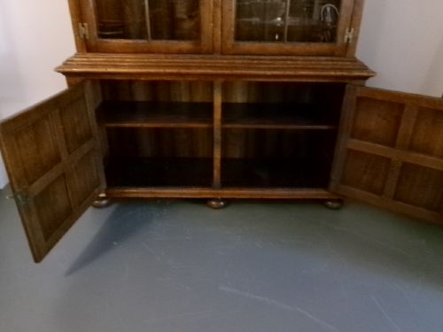 A large two-section warm brown oak bookcase featuring two upper glazed doors with internal shelves above two lower field-panelled wooden doors. View III