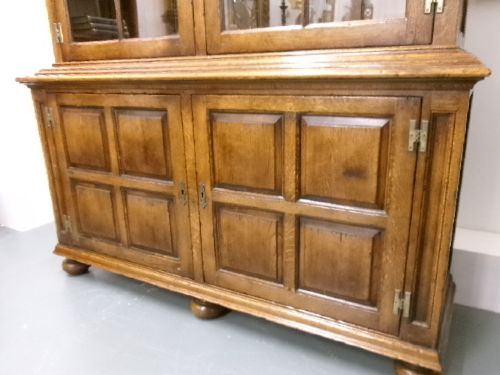 A large two-section warm brown oak bookcase featuring two upper glazed doors with internal shelves above two lower field-panelled wooden doors. View X