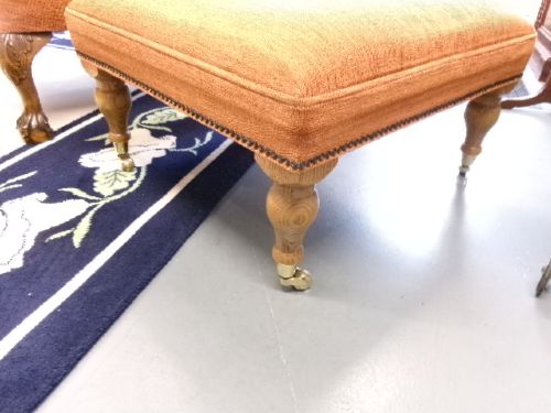 A high-backed Georgian style wing armchair with rolled arms, upholstered in textured orange fabric, accompanied by a matching square footstool. View II