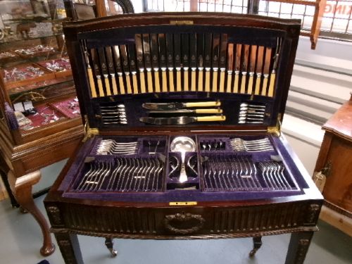 A dark mahogany freestanding cutlery cabinet with a open hinged lid displaying a fitted purple velvet interior with silver-plated flatware. View IV