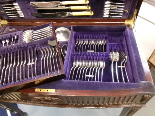 A dark mahogany freestanding cutlery cabinet with a open hinged lid displaying a fitted purple velvet interior with silver-plated flatware. View V