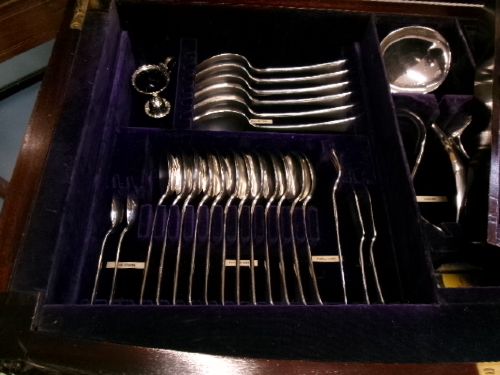 A dark mahogany freestanding cutlery cabinet with a open hinged lid displaying a fitted purple velvet interior with silver-plated flatware. View VII