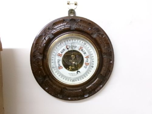 A circular Edwardian aneroid barometer set within a hand-carved mahogany frame with a brass bezel and visible mechanical movement. View III