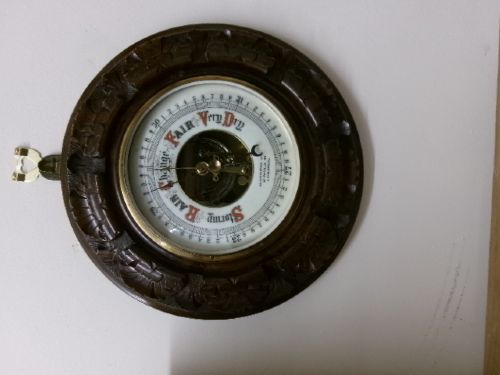 A circular Edwardian aneroid barometer set within a hand-carved mahogany frame with a brass bezel and visible mechanical movement. View IV