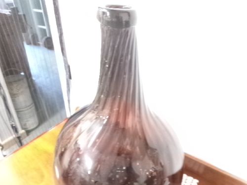 A deep amethyst hand-blown glass bottle featuring a bulbous onion-shaped body, a spiral-ribbed tapering neck, and an applied string lip rim. View IX