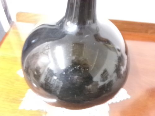 A dark green hand-blown glass onion bottle featuring a broad bulbous body, a long tapered neck, and an applied glass string rim. View III