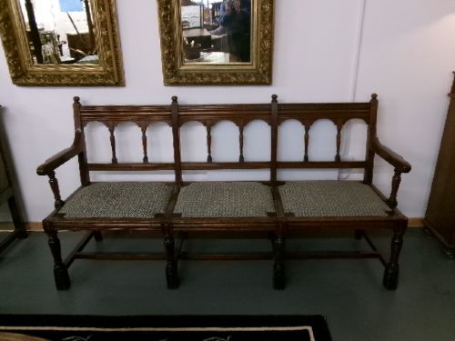 A late Victorian carved walnut three-seater bench featuring an arched spindle backrest, armrests, upholstered seat pads, and turned front legs. View II