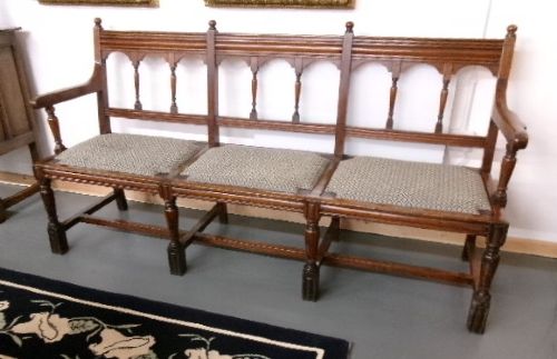 A late Victorian carved walnut three-seater bench featuring an arched spindle backrest, armrests, upholstered seat pads, and turned front legs. View IV